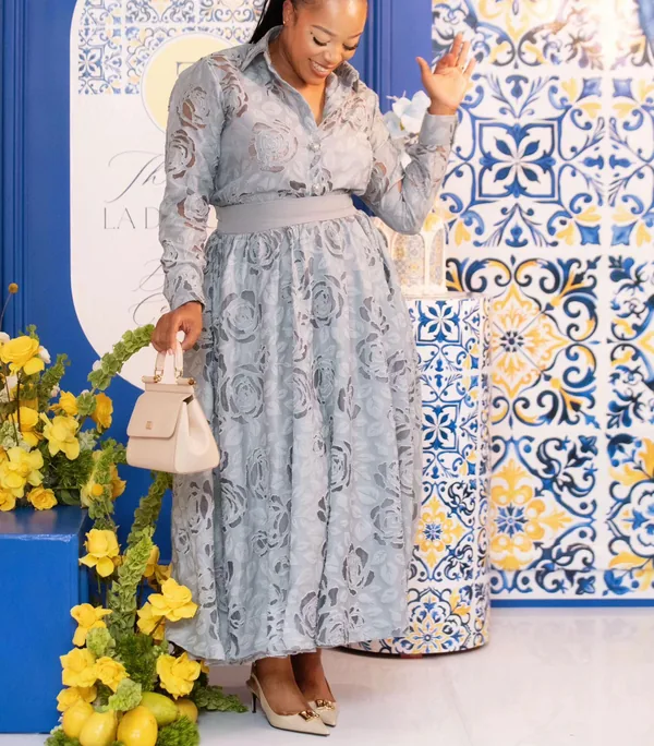 MaShandu in a grey lace dress in front of blue and yellow tiles
